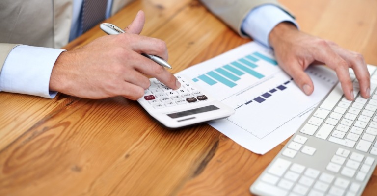 Man with a calculator, data sheets, and computer keyboard, suggesting business valuation